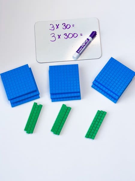 Small whiteboard with a math problem next to several sets of base-ten blocks for teaching the value of digits in math
